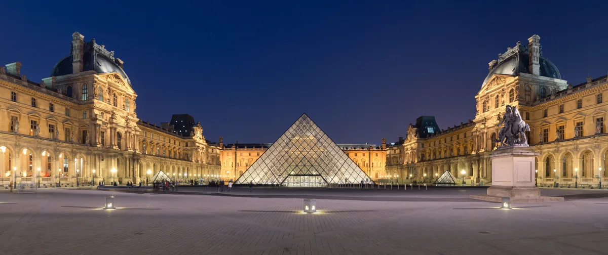 Skutečná fotografie osvětlené pyramidy a nádvoří Louvru v Paříži